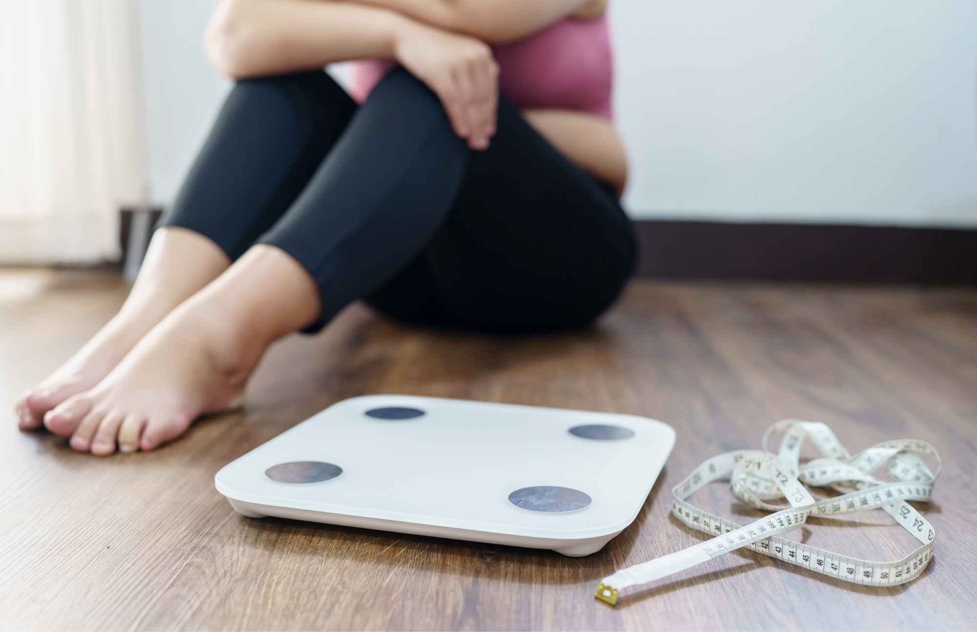 Frustrated woman sitting beside a scale and measuring tape, highlighting weight gain challenges linked to hormonal changes.