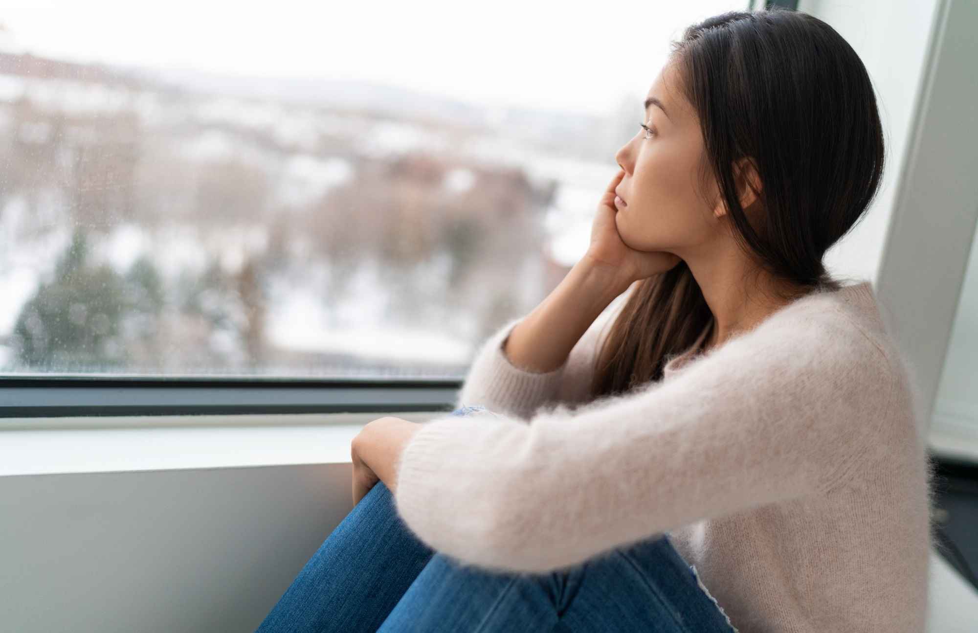 Woman gazing out the window, looking sad and distant, symbolizing mood swings and depression caused by hormonal imbalance.