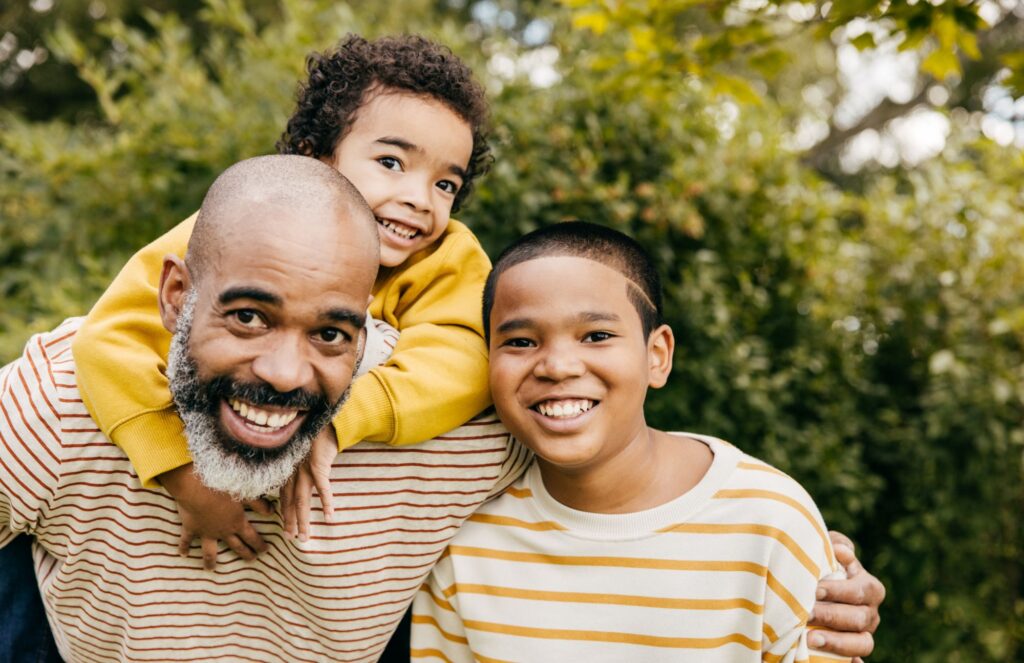 A smiling father with his two children outdoors, symbolizing strong immunity and overall health benefits from Vitamin D.
